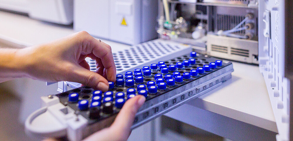 A scientist prepares to load liquid samples into a High-Performance Liquid Chromatography machine for analysis